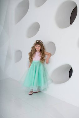 Nane elbiseli güzel küçük kız. Bir çelenk ve çiçek beyaz odasındabir kızla