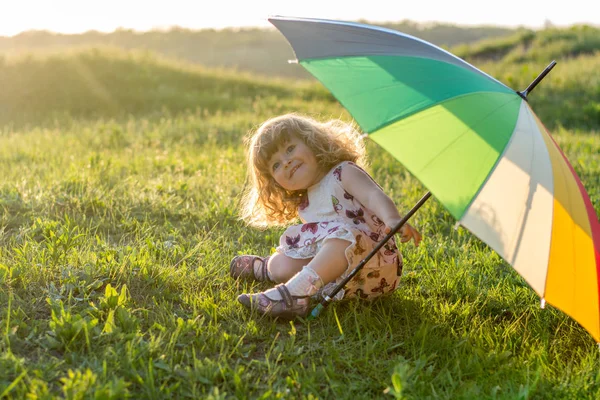 Beautiful girl plays on nature with a colorful umbrella. Rainbow umbrella in the hands of the child