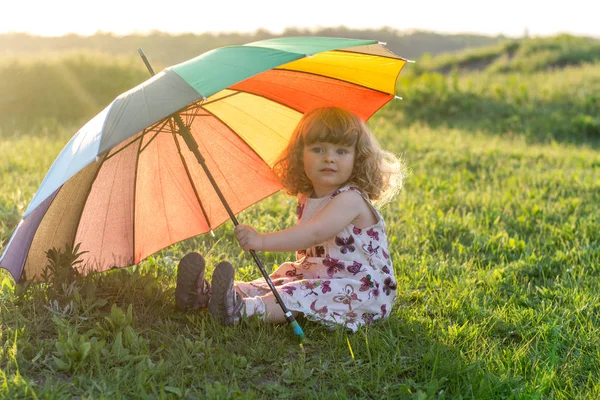 Beautiful girl plays on nature with a colorful umbrella. Rainbow umbrella in the hands of the child