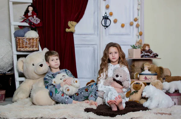 Children play sitting on the floor in their pajamas. The boy and the girl laugh and throw soft bears. pajama party
