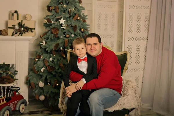 father and son sitting near Christmas tree