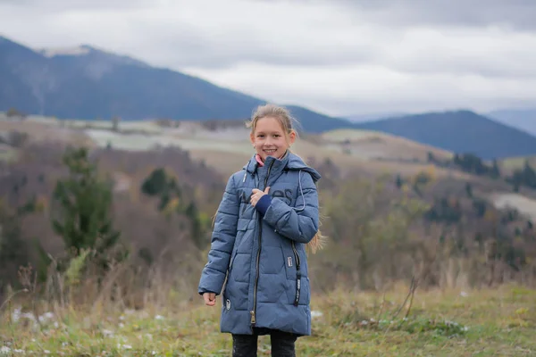 The child is smiling and happy against the backdrop of the mountains. Travel to the mountains. Girl happy in the mountains