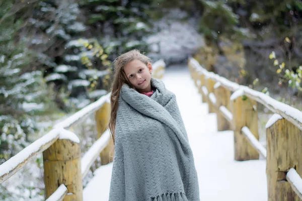 美丽的女孩长头发站在雪树林里 孩子被毯子包裹着 桥上的雪 — 图库照片