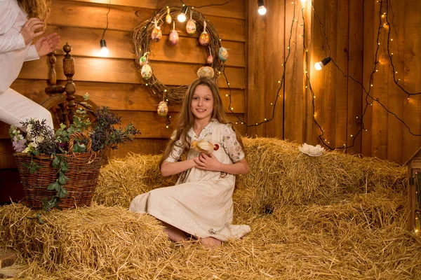 女の子は笑い 彼女の手に鶏を保持します その子は干し草の山の中に座っている 動物と田舎で長い髪を持つ美しい子供 — ストック写真