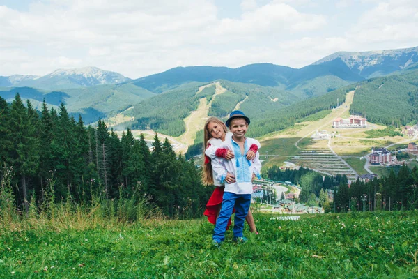 Brother and sister in national clothes in the mountains. Children travel. Beautiful boy and beautiful girl smiling in nature