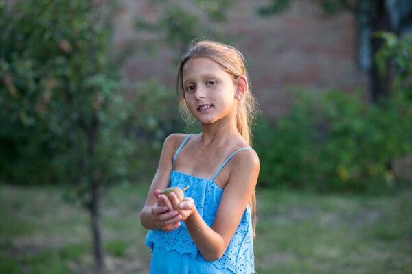 A beautiful long-haired girl picks pears in the garden. The child is holding a pear. The girl smiles and picks pears. Harvesting