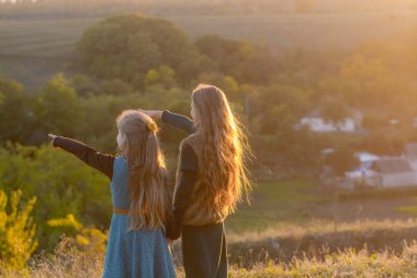 Doğada sonbaharda gün batımında iki küçük kız kardeş. Küçük kız kardeşler yalnız. Güzel uzun saçlı kızlar ve sonbahar doğası