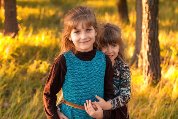 Two little sisters hugging in an autumn park. Children are smiling and happy in nature. Beautiful long-haired sisters