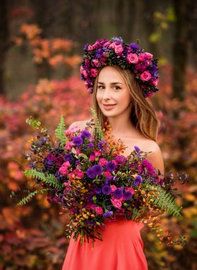 Çelenk takmış güzel bir genç kadın ve sonbahar parkında bir buket çiçek. Güzel çiçekçi kız..