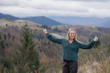 Güzel bir Moldova kadını, arka planda kalan dağlarda gülümsüyor. Sonbahar dağlarında bir kızın portresi. Uzun sarı saçlı bir kadın.