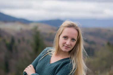 Güzel bir Moldova kadını, arka planda kalan dağlarda gülümsüyor. Sonbahar dağlarında bir kızın portresi. Uzun sarı saçlı bir kadın.