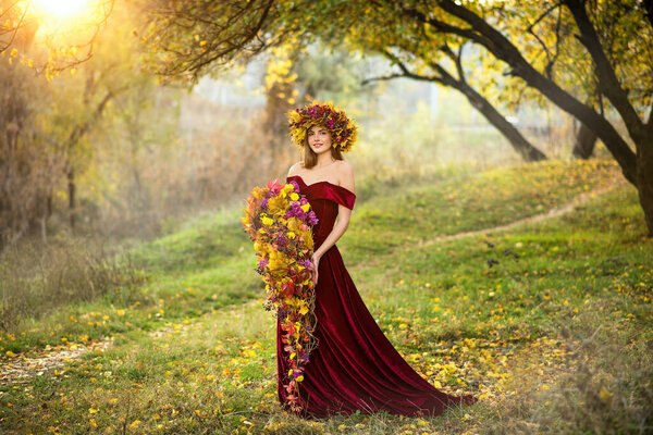 Beautiful young woman in an autumn park in a long dress. Girl with an autumn bouquet in her hands. The woman has a wreath of flowers on her head. Autumn floristry