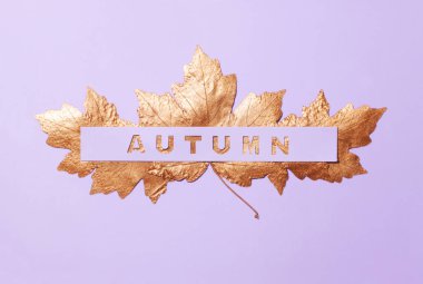 Kavramsal yazıt Altın yaprağı altında gördüğünüz bir menekşe arka planda sonbahar oyulmuş.