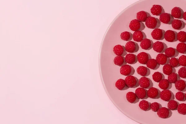 明亮成熟多汁的覆盆子在柔和的粉红色盘子上柔和的浅蓝色背景 — 图库照片