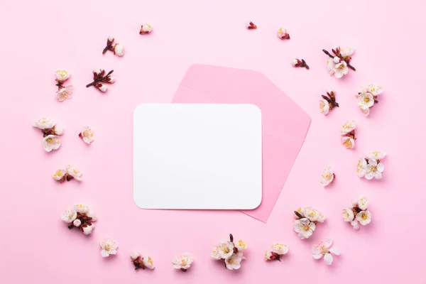 春の花で飾られたピンクの紙の背景の中に白いステッカーが付いているピンクの封筒. — ストック写真