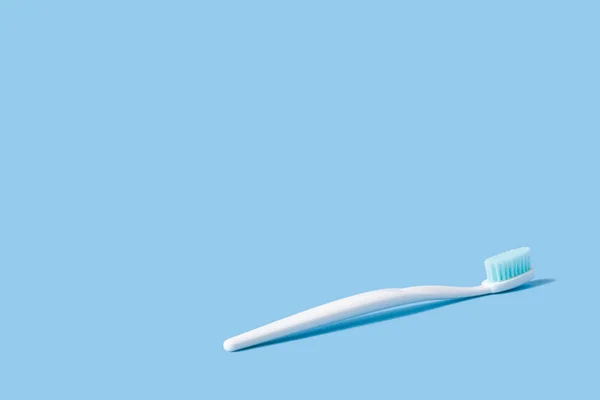White toothbrush with blue bristles on a pink paper background decorated with spring flowers. — Stock Photo, Image