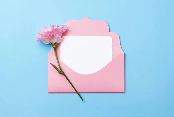 Růžová obálka s bílým nálepkou na růžovém papíru ozdobená jarním květinami. — Stock fotografie