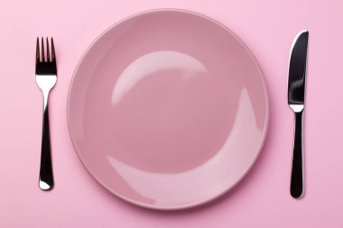 Pembe, parlak, metal çatal bıçaklı bir tabak. Pembe kâğıt üzerinde çatal ve bıçak..