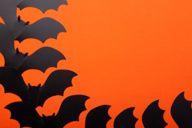 Siyah el, turuncu arka planda kağıt yarasa yapmış..