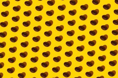 Seçilmiş kahve çekirdeklerinin gerçek makro fotoğraflarından oluşan yaratıcı parlak kolaj sarı bir zemin üzerinde, kalp şeklinde sert bir gölge ve yazıtlar için yeri var..