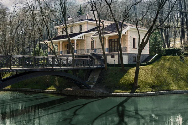 Bulutlu bir sonbahar gününde nehir kenarında köprüsü olan taş bir ev.