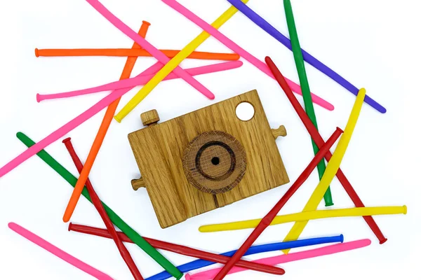 Beyaz arka planda ahşap kamera, renkli çizgili toplarla çevrili..