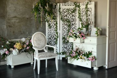 Fotoğraf stüdyosunda sandalye ve çiçek dekoru olan beyaz bir iç mekan.