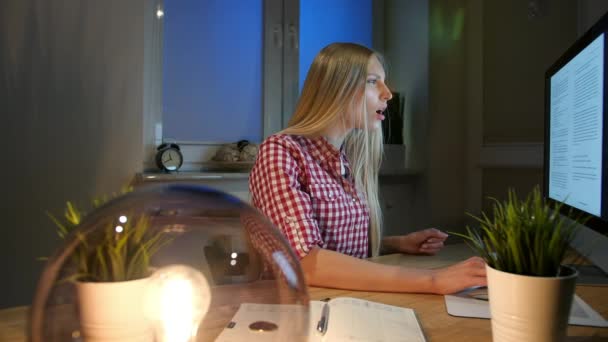 Ελκυστική γυναίκα κατάπληκτη από τις πληροφορίες στην οθόνη. Όμορφη νεαρή ξανθιά γυναίκα ευτυχώς παλαμάκια χέρια και ψάχνει με ανοιχτό το στόμα σε οθόνη υπολογιστή στο ξύλινο γραφείο κάθεται στο σκοτεινό δωμάτιο τη νύχτα — Αρχείο Βίντεο