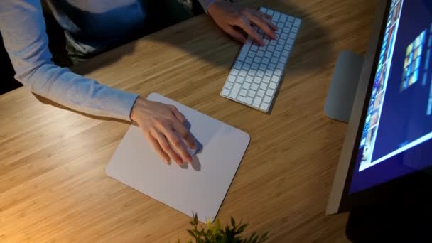 Una donna che lavora al computer di notte. Crop vista delle mani della donna in comodi vestiti di casa seduto alla scrivania di legno acceso dalla lampada e utilizzando il mouse del computer e la tastiera in camera oscura di notte . — Video Stock