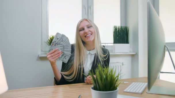 Lächelnde Geschäftsfrau mit einem Bündel Bargeld. schöne glückliche blonde Frau sitzt im Büro am Arbeitsplatz mit Computer und hält Fan von Banknoten und schaut in die Kamera lächelnd. — Stockvideo