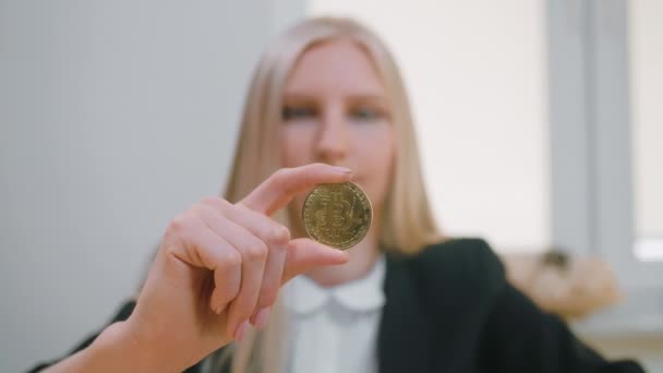 Mulher feliz com bitcoin mostrando polegares para cima. Sorrindo alegre mulher loira em terno de escritório sentado no local de trabalho com computador e mostrando bitcoin na mão fazendo polegares acima gesto e olhando para a câmera — Vídeo de Stock