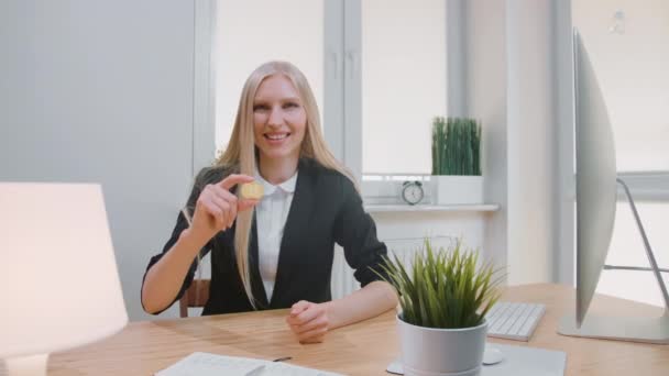 Gelukkige vrouw met bitcoin duimen opdagen. Vrolijke blonde vrouw in office pak zitten op de werkplek met computer tonen bitcoin girosaldi doen duimen omhoog gebaar en kijken naar camera glimlachen — Stockvideo