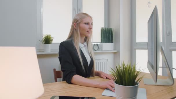 Leende affärskvinna som visar tummen upp. Glada ung blond kvinna i elegant kostym sitter på kontoret vid skrivbordet med dator och gör tummen upp gest tittar på kameran och ler. — Stockvideo