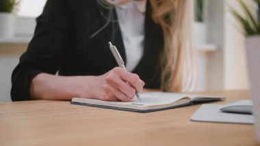 Güzel genç sarışın kadın uygun kalem, Not Defteri'nde ile yazma, sayfa dönüm ve yaprak kağıt defterini dan çekerek masada oturma.