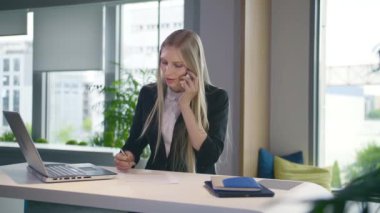 Moda bir iş kadını dizüstü bilgisayar izliyor ve telefonda konuşuyor. Masa başı bilgisayarında çalışan zarif sarışın kadın ve gülümserken telefonla arayan kadın..