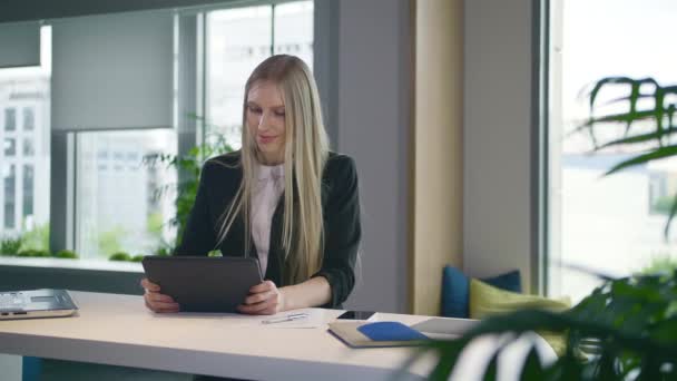 Elegante mujer de negocios con tableta en la oficina. Mujer elegante en traje sentado en la mesa con ordenador portátil y tableta de surf en la oficina de luz moderna con grandes ventanas . — Vídeos de Stock