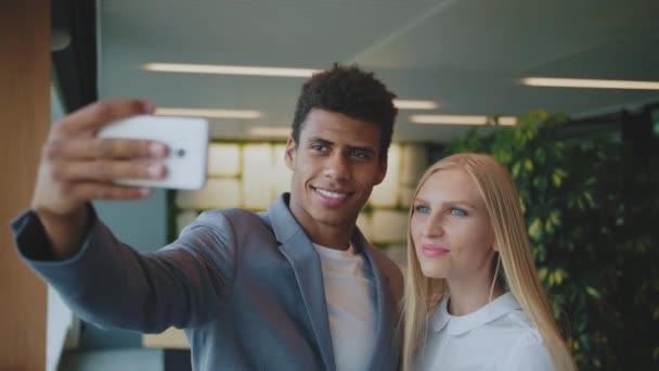 Gülen çeşitli iş arkadaşları ofiste selfie çekiyorlar. Neşeli siyah adam ve gülen sarışın kadın modern ofiste akıllı telefonuyla selfie çekiyorlar. — Stok video