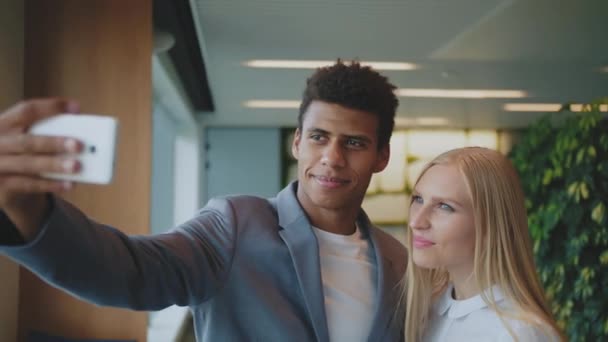 Lachen diverse collega 's nemen selfie in het kantoor. Vrolijke zwarte man met lachende blonde vrouw nemen selfie met smartphone in modern kantoor hebben plezier — Stockvideo