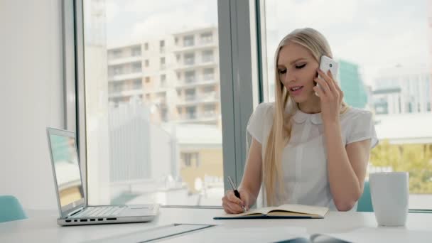 Serieuze vrouw die in een lichte kantoorruimte werkt. Elegante moderne zakenvrouw met laptop en papieren aan lange tafel in conferentie lichte kamer met telefoontje. — Stockvideo