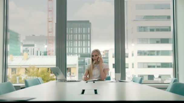 Geschäftsfrau winkt mit der Hand, während sie telefoniert. stylische Geschäftsfrau telefoniert, während sie am Tisch im Konferenzsaal sitzt und mit händchengrüßenden Kollegen winkt. — Stockvideo