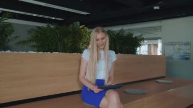 Ofiste tablet ile rahatlatıcı bir kadın. Çıplak ayakla tablet ve alarak dinlenme kullanarak modern ofis ahşap kürsü üzerinde oturan genç zarif kadın.