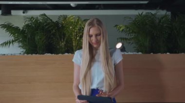 Ofiste tablet ile rahatlatıcı bir kadın. Çıplak ayakla tablet ve alarak dinlenme kullanarak modern ofis ahşap kürsü üzerinde oturan genç zarif kadın.