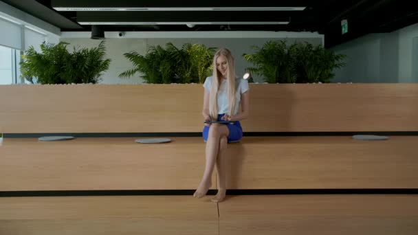 Femme détendue avec tablette au bureau. Jeune femme élégante assise pieds nus sur tribune en bois dans un bureau moderne en utilisant une tablette et en prenant du repos . — Video