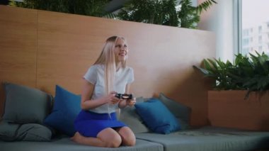 Oyun ve modern ofiste rahatlatıcı bir kadın. Divan çağdaş ofis rekreasyon alanı içinde soğutma ve gamepad ile video oyunu oynarken etekle genç resmi kadın.