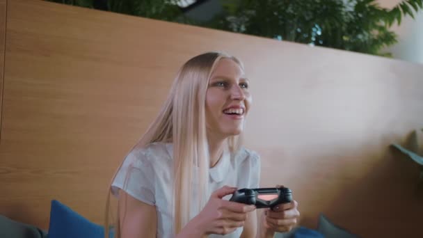 Kobieta, gier i zrelaksować się w nowoczesnym biurze. Młoda kobieta formalne w spódnicy chłodzenie na kanapie w strefie rekreacyjnej nowoczesne biuro i odtwarzanie gier wideo z gamepad. — Wideo stockowe