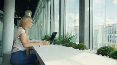 Resmi ve kadın ile dizüstü bilgisayar kağıtları. İş kadını ile laptop modern ofis penceresinde yakınındaki masada otururken kağıda yazı yan görünüm.