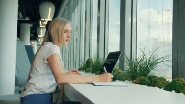 Resmi ve kadın ile dizüstü bilgisayar kağıtları. İş kadını ile laptop modern ofis penceresinde yakınındaki masada otururken kağıda yazı yan görünüm.