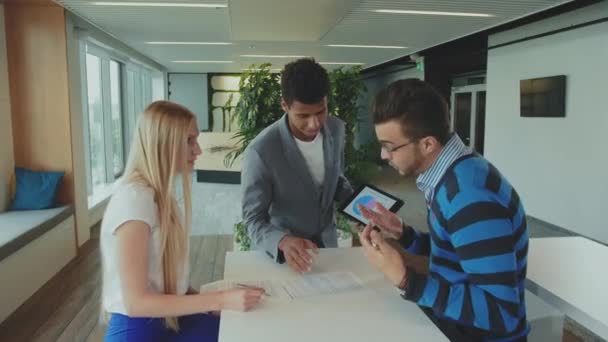 Männer und Frauen unterschiedlicher Rassen arbeiten an Berichten. Gruppe unterschiedlicher Frauen und Männer mit Tablet im modernen Bürosaal, die mit Dokumenten und Statistiken arbeiten. — Stockvideo