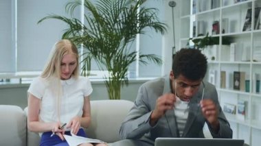 Siyahi adam iş arkadaşlarıyla iyi haberleri paylaşıyor. Afro-Amerikalı adam dizüstü bilgisayarda sörf yapıyor ve harika haberleri iş arkadaşlarıyla paylaşıyor. Masanın etrafında birlikte oturuyorlar..