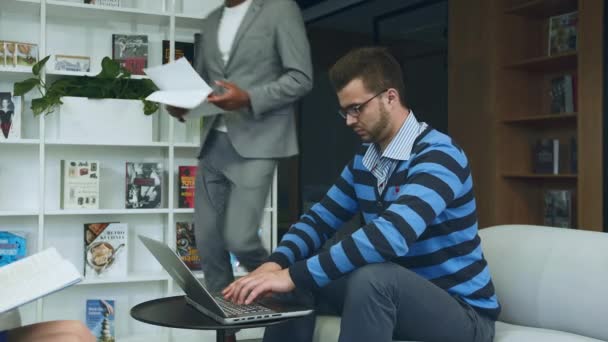 Des collègues avec des papiers et un ordinateur portable. Vue latérale de divers hommes et femmes se réunissant sur le canapé dans le bureau avec ordinateur portable et papiers ayant réunion . — Video